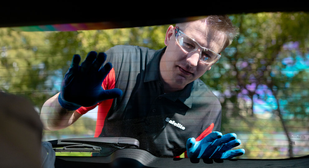 A Safelite technician in gloves taking a close look at rear window glass work.