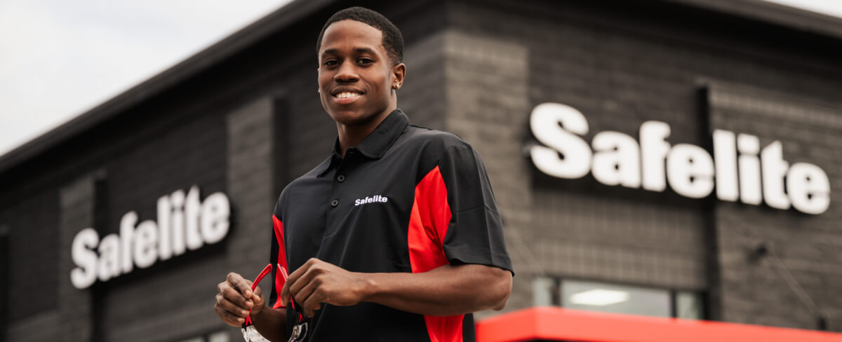A Safelite technician smiling in front of a Safelite shop
