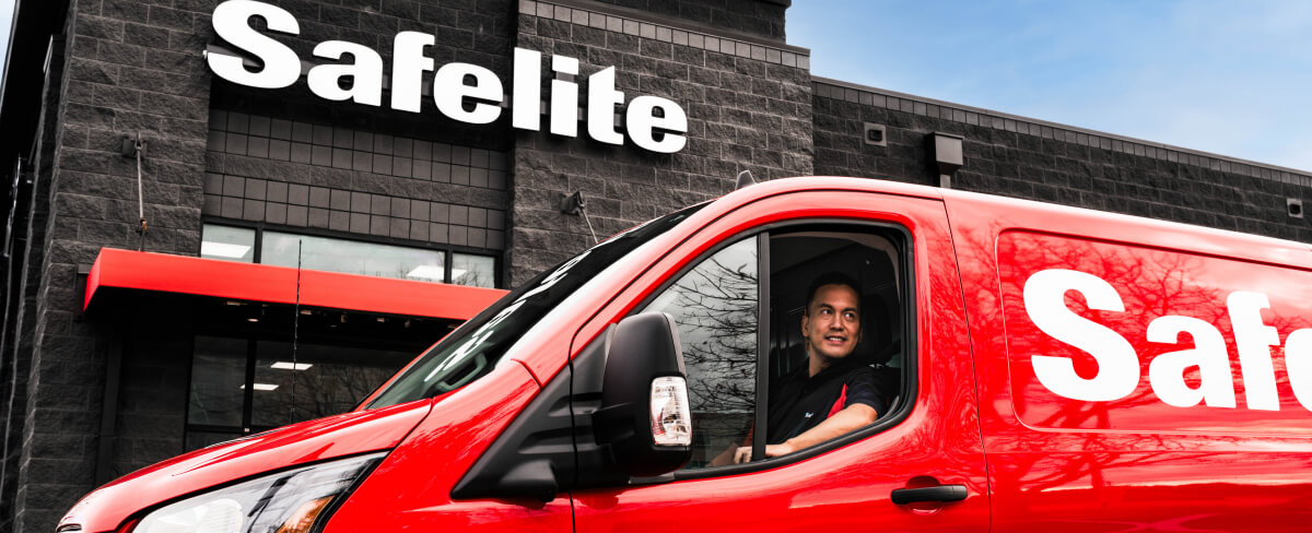 A Safelite technician in a mobile glass shop vehicle in front of a Safelite shop